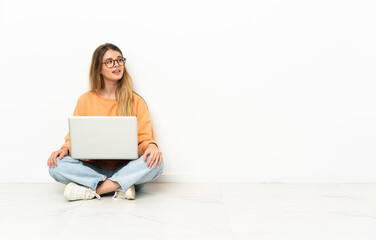 Young woman with a laptop sitting on the floor looking to the side