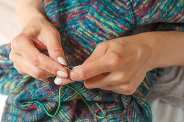 Close up of hands of unrecognizable woman knitting handmade clothes with spokes using  wool yarn. Concept of leisure activity.Knitting from yarn on  coarse spokes.