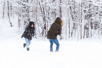 Fototapeta na wymiar Lifestyle, season and leisure concept - Funny couple playing snowball in winter park