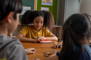 Serious African American school girl looking at children in classroom, playing a game, challenge, learning, counting. School girl with hands on table concentrating during challenge