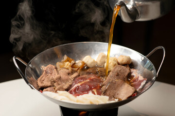 Chef pouring aromatic broth to fine sliced beef