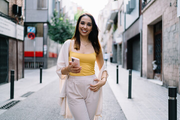 Smiling woman messaging on phone while walking on street