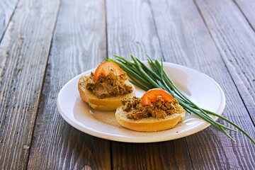 Homemade pate of pig or chicken liver on wheat buns on a white ceramic plate on brown wooden background.