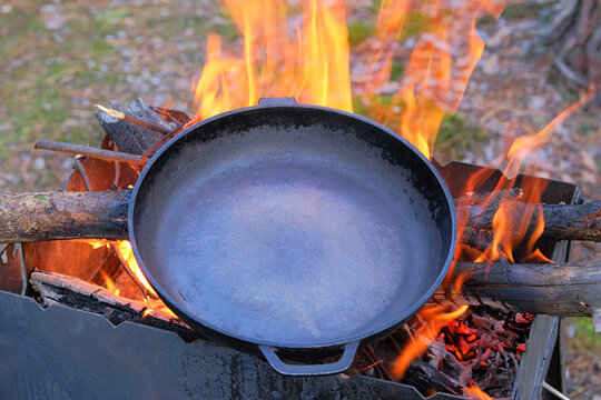 Сast Iron Skillet Over An Red Fire Heats Up For Further Cooking. Firing A Cast Iron Skillet Over An Open Fire.