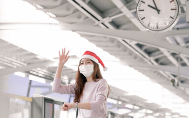 Woman wearing santa hat and mask to protect virus and standing on railway station