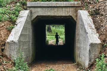 Curious boy on a bike rides into a dark tunnel under the railway