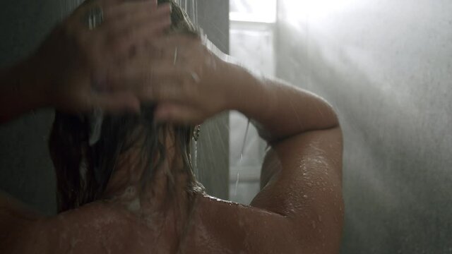 Close-up back shot of a woman taking a shower and washing her hair with shampoo