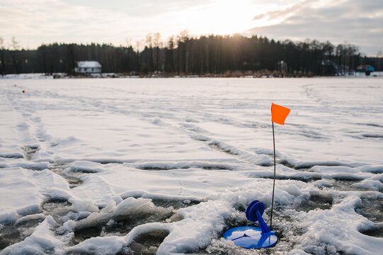 Just Caught Pike By Tip - Up Tackle. In The Ice Hole Set Tackle With A Flag. Winter Fishing On The Frozen Lake. Small Tackle For Winter Fishing On The Ice Pond. Reeling Reel For A Fish.