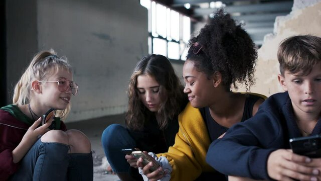 Group of teenagers gang with smartphone indoors in abandoned building, looking at camera.