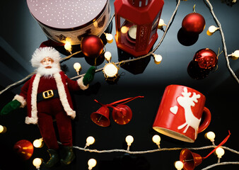 Top view of Christmas decorations with Santa, gift box, cup, lights and lantern on black background.
