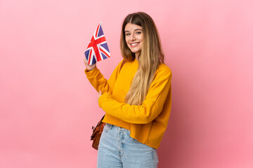 Young blonde woman holding an United Kingdom flag isolated on white background pointing back