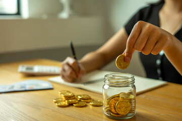Fototapeta na wymiar Woman taking note And make income and expenditure accounts by inserting coins in the savings To save money Keep it as retirement money, ideas for saving money for the future