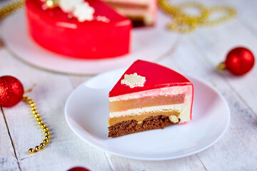 Mousse Christmas pastry cake dessert covered with red mirror glaze with new year decorations on garland lamps bokeh white background, Modern european cake Christmas theme. .