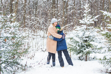Fototapeta na wymiar Fun and season concept - Happy mother and son having fun and playing with snow in winter forest