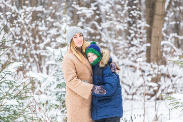 Portrait of happy mother with child son in winter outdoors. Snowy park. Single parent.