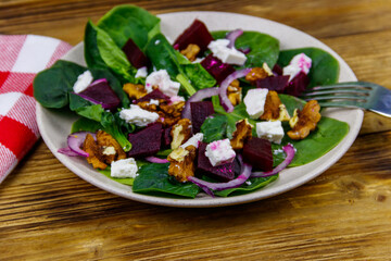 Tasty spinach salad with boiled beetroot, feta cheese, walnut and red onion on wooden table. Healthy vegetarian food