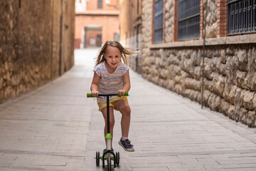 blonde girl running on three-wheeled scooter.