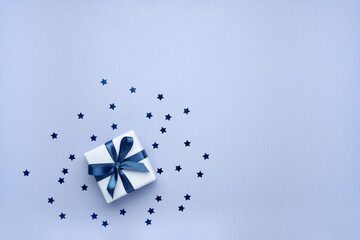 Gift box with ribbon and bow on blue background with stars  shaped confetti. Top view and space for...
