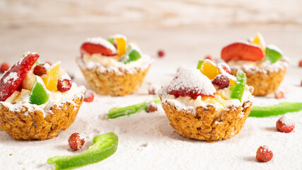 Oat cupcakes with cottage cheese filling. Red strawberry, yellow and green dried fruits and icing sugar sprinkled around
