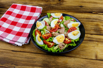 Tasty tuna salad with eggs, lettuce and fresh vegetables on wooden table
