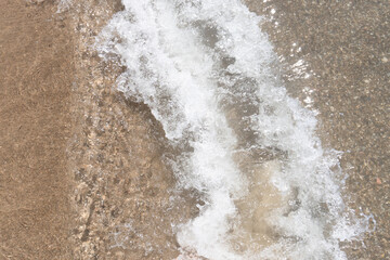 Ocean waves low tide at the beach. White bubbles. Windy sea. Sea waves on the pebble beach