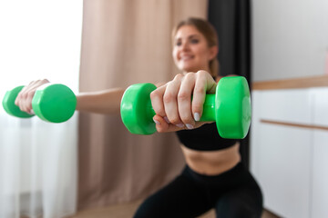A woman performs weighted squats. Dumbbells in the hands of a girl close up