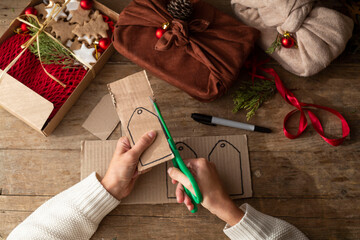 female hands in a white sweater keep eco frindly packed gift with tags from craft cardboard....