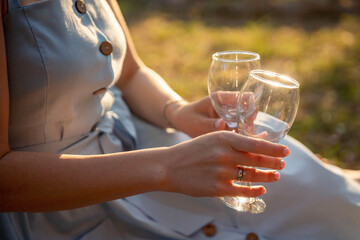 female hands holding wine glasses, sunset sun light, picnic at sunset in the park