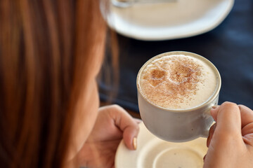 Top view back, Hot cappuccino coffee in woman hand.