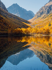 Mountain lake with transparent water, reflection and colorful autumnal trees.