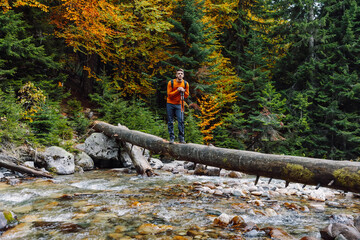 Hiker man on a log over the river in autumnal mountains. Mountain river and hiker