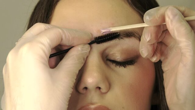 Correction of a shape of eyebrows with hot wax close up. Brow master applying wax on the eyebrow of female face of a brunette woman. Wax correction of the shape of the eyebrows with spatula. Beauty in