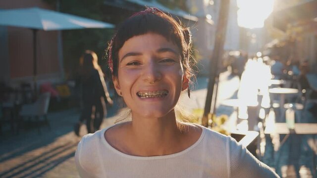 Toothy smile. Close up portrait of funny caucasian travel woman smiling into camera and showing teeth with braces while having fun, laughing on the street of old city with beautiful golden sunset
