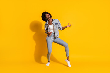 Fototapeta na wymiar Full length photo of lovely adorable young lady wear casual denim outfit dancing pointing empty space isolated yellow color background