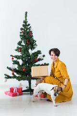 Happy young woman with lovely dog opening present box under christmas tree. Holidays concept.