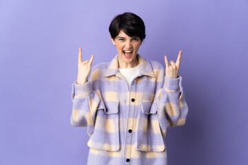 Woman with short hair isolated on purple background making horn gesture