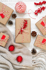 Top view of handcrafted gifts. Christmas flat lay with pine cones, presents wrapped in craft paper and decorated with striped baker's twine string and holly berries on the wooden background.