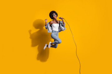 Full body photo of cheerful pretty crazy lady jump air sing song microphone wear jeans singlet...