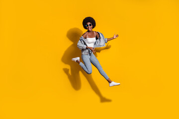 Full length photo of stylish trendy girl play guitar jump up wear denim pants singlet isolated on yellow color background