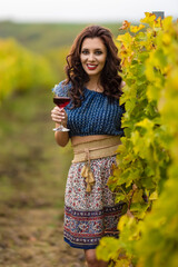 A beautiful woman with a glass of red wine in the vineyard on autumn day.