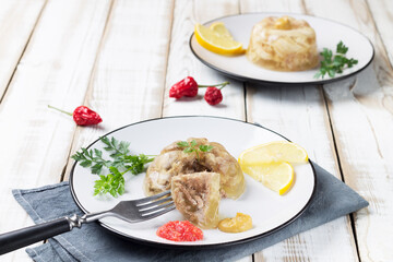 Two plates of cold beef and chicken with lemon slices, mustard and adjika. Natural wooden background.