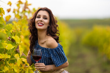 A beautiful woman with a glass of red wine in the vineyard on autumn day.