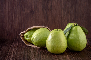Close up of delicious guava with fresh green leaves on wooden background.