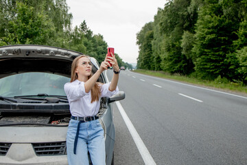 Young woman standing near broken down car with popped up hood having trouble with her vehicle....