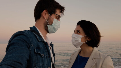 Ragazzo e ragazza si bacia con la mascherina in riva al mare