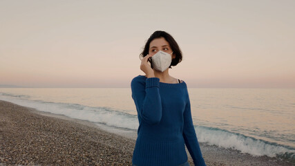 Giovane ragazza con maglia blu e mascherina passeggia in riva al mare
