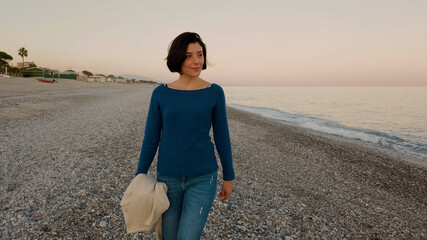 Ragazza con maglia blu e giacca marrone passeggia in riva all'oceano