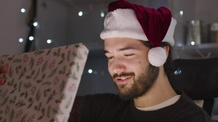Male opening Christmas present which lights up while wearing a Christmas hat