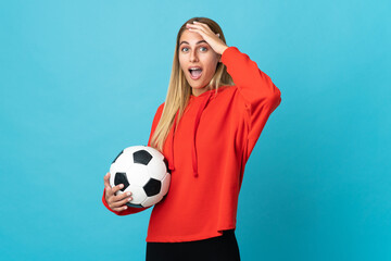 Young football player woman isolated on blue background doing surprise gesture while looking to the side