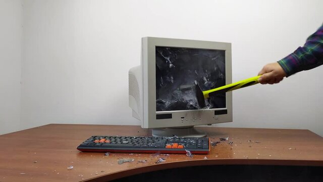 An old monitor sitting on a table is smashed with a hammer. The shattered glass of the monitor is flying in all directions. 4k